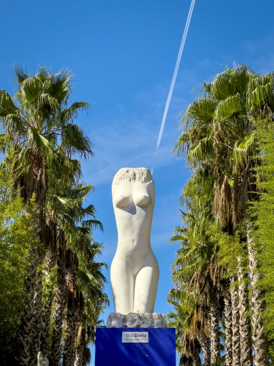 White female figure sculpture by Bia Doria among palm trees