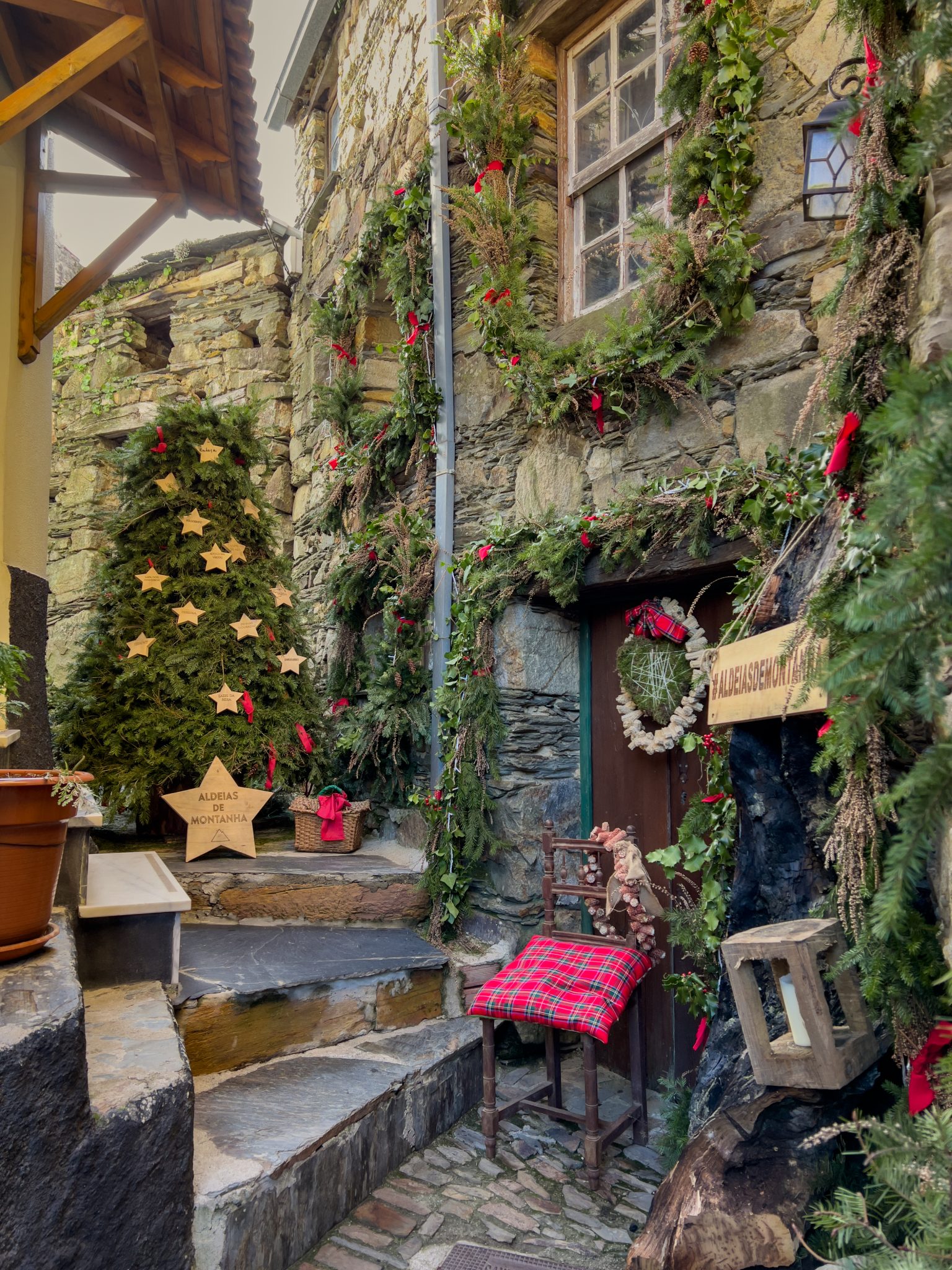 Traditional Mountain Christmas Stone house entrance decorated with natural wreaths, wooden stars and tartan cushions